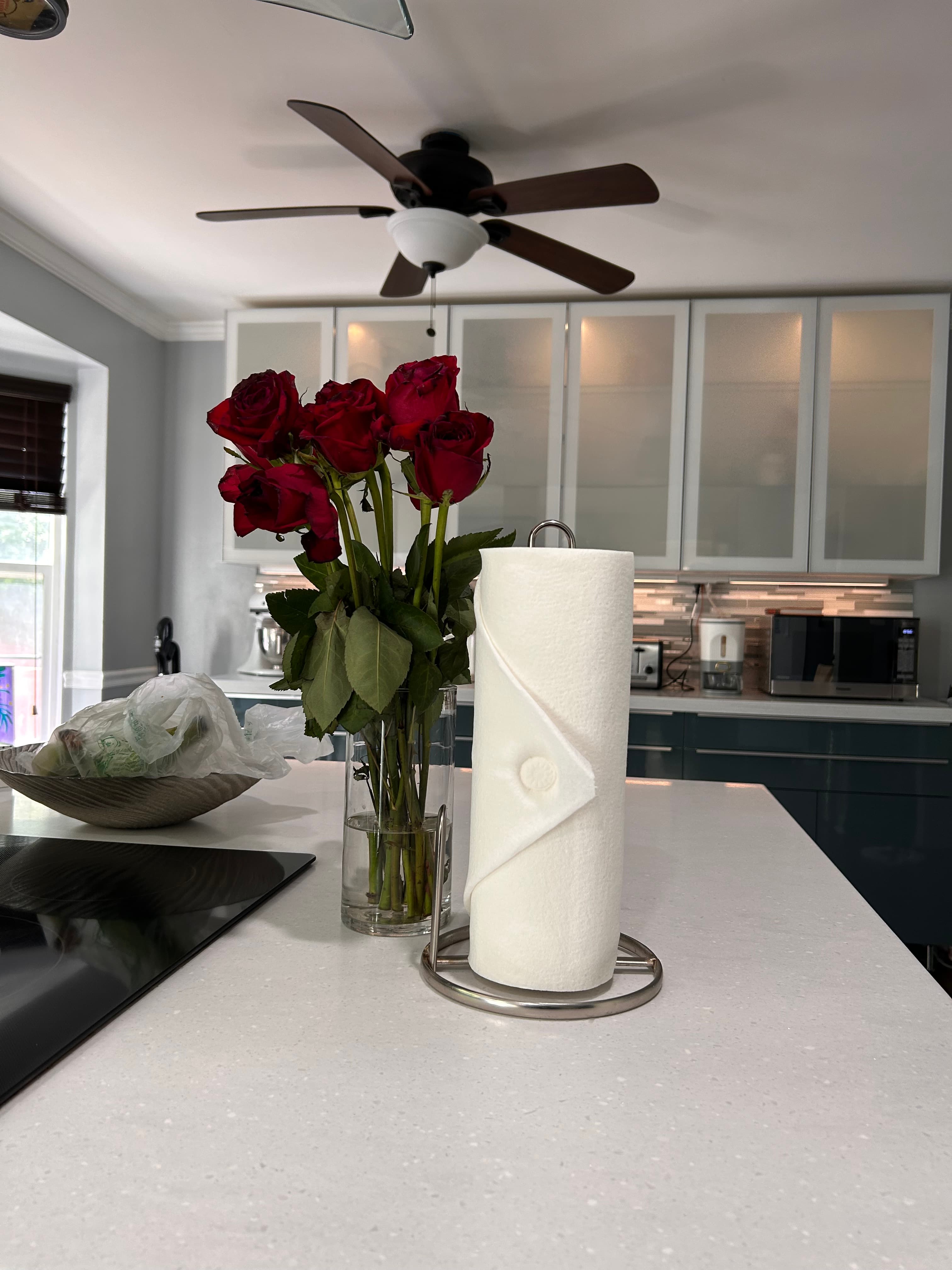 Red roses in a vase beside a paper towel roll on a white kitchen countertop.