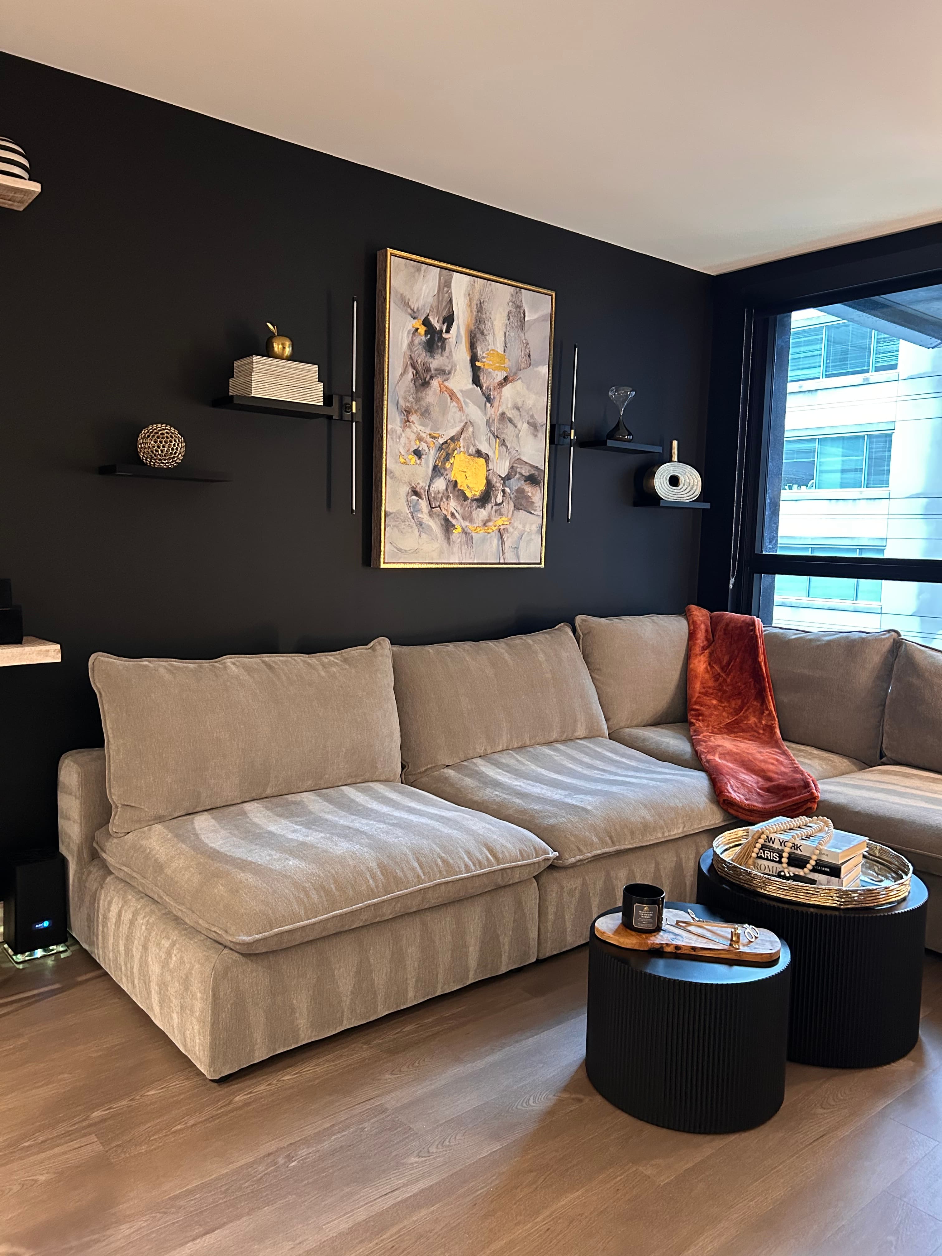 Modern living room with a grey sectional sofa, black accent wall, and abstract gold-flecked art.