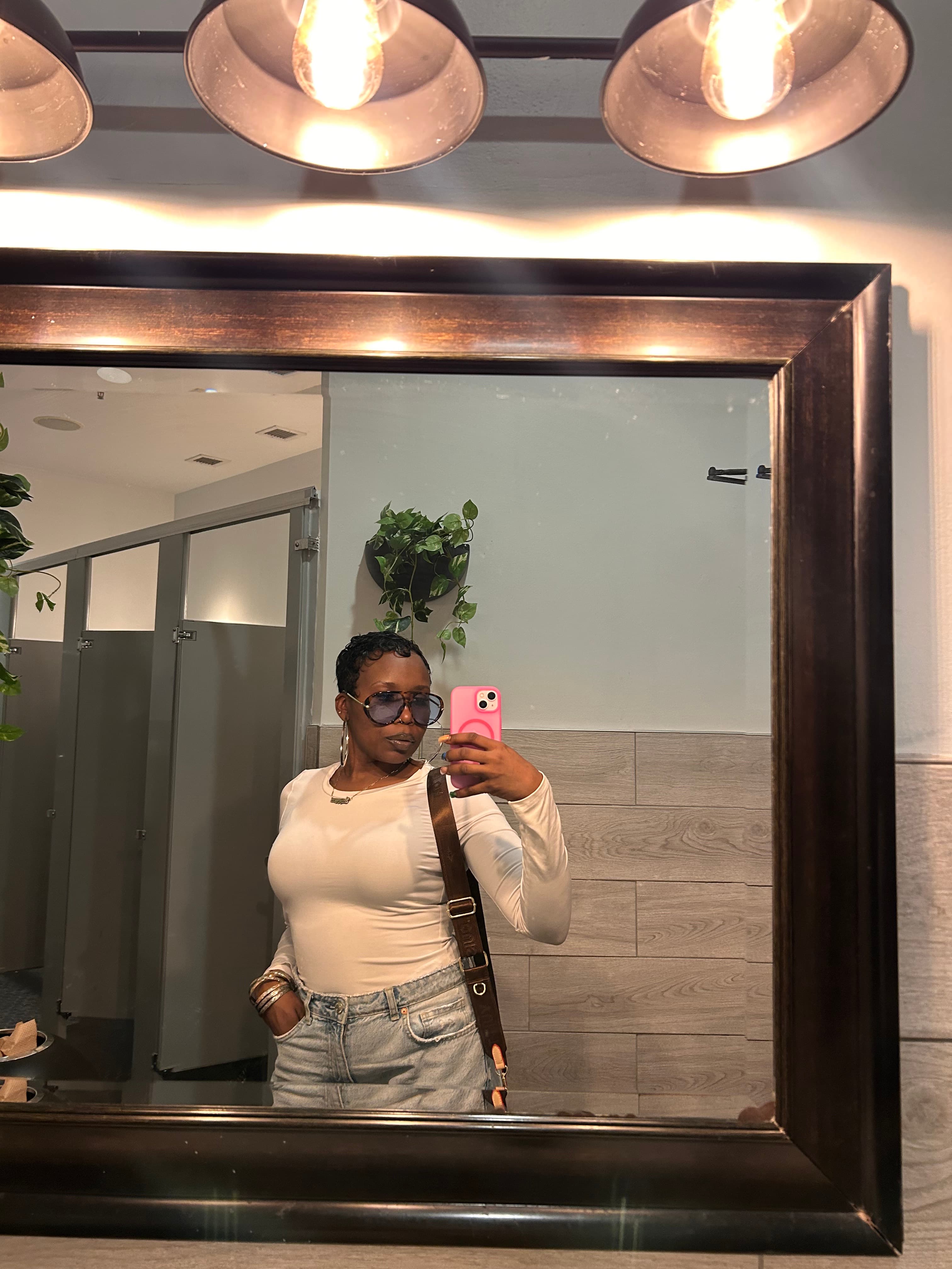 Woman in sunglasses and white top takes a mirror selfie with a pink phone.