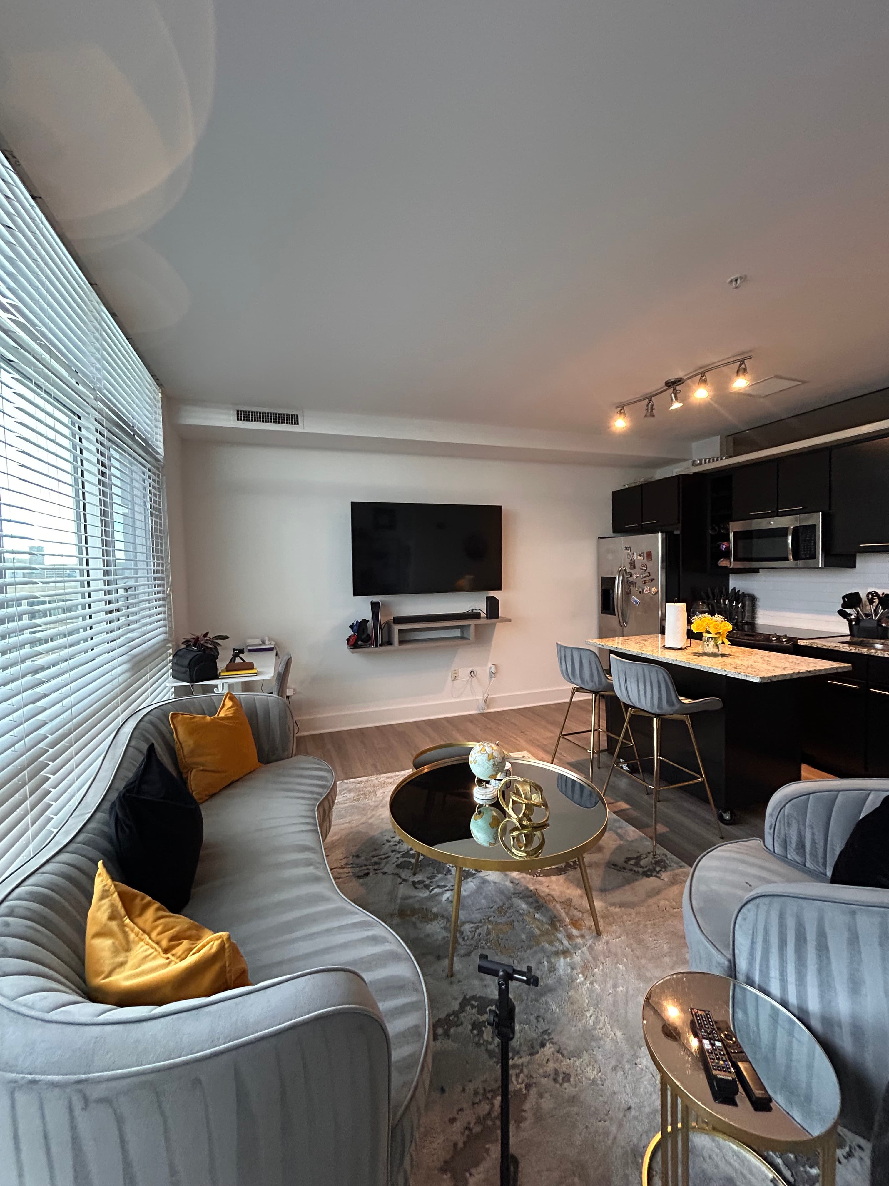Modern living room with a curved gray sofa, gold coffee table, and dark open kitchen.