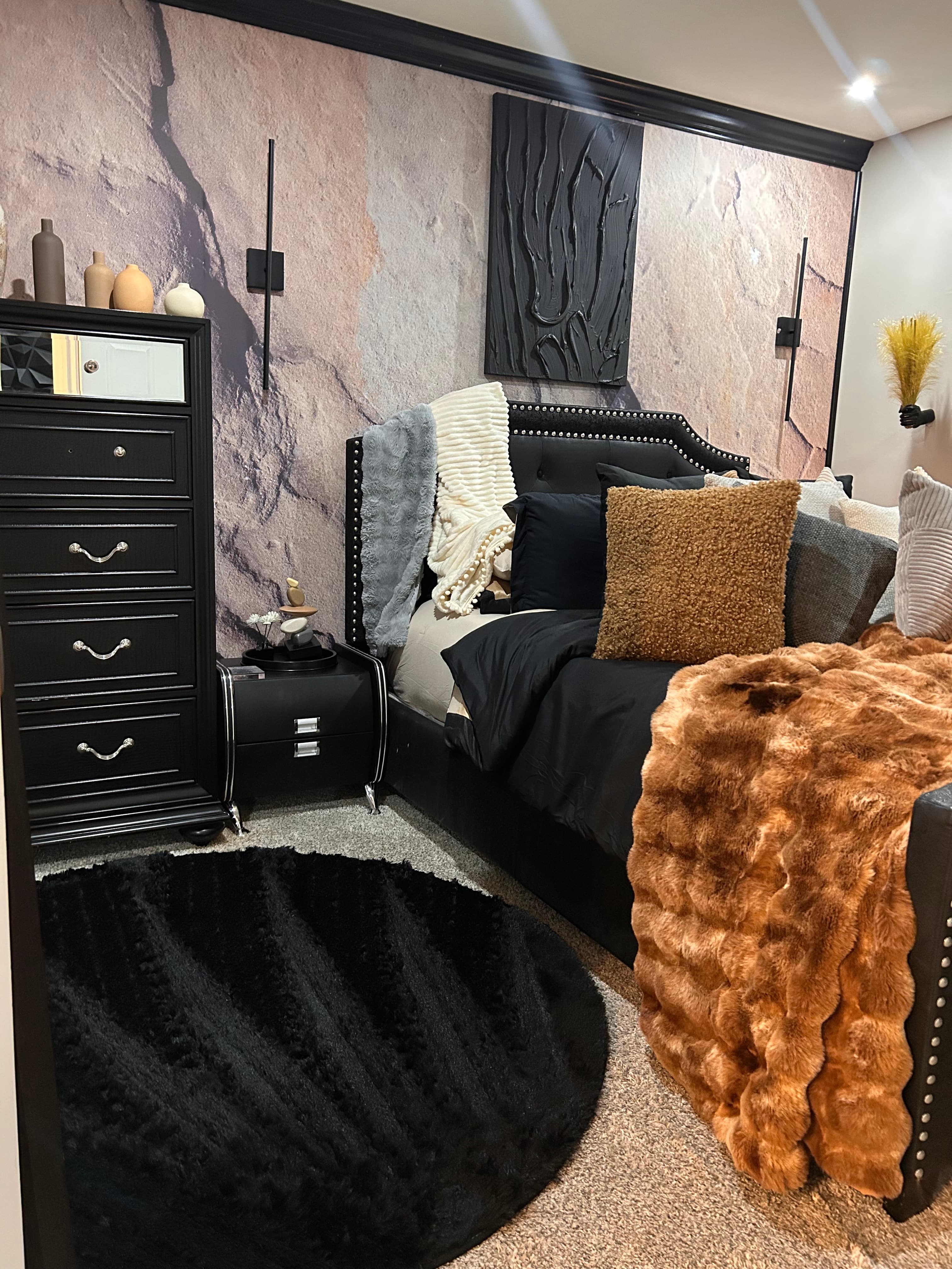 Modern bedroom featuring a black tufted bed, brown fur throw, and stone-textured wall mural.