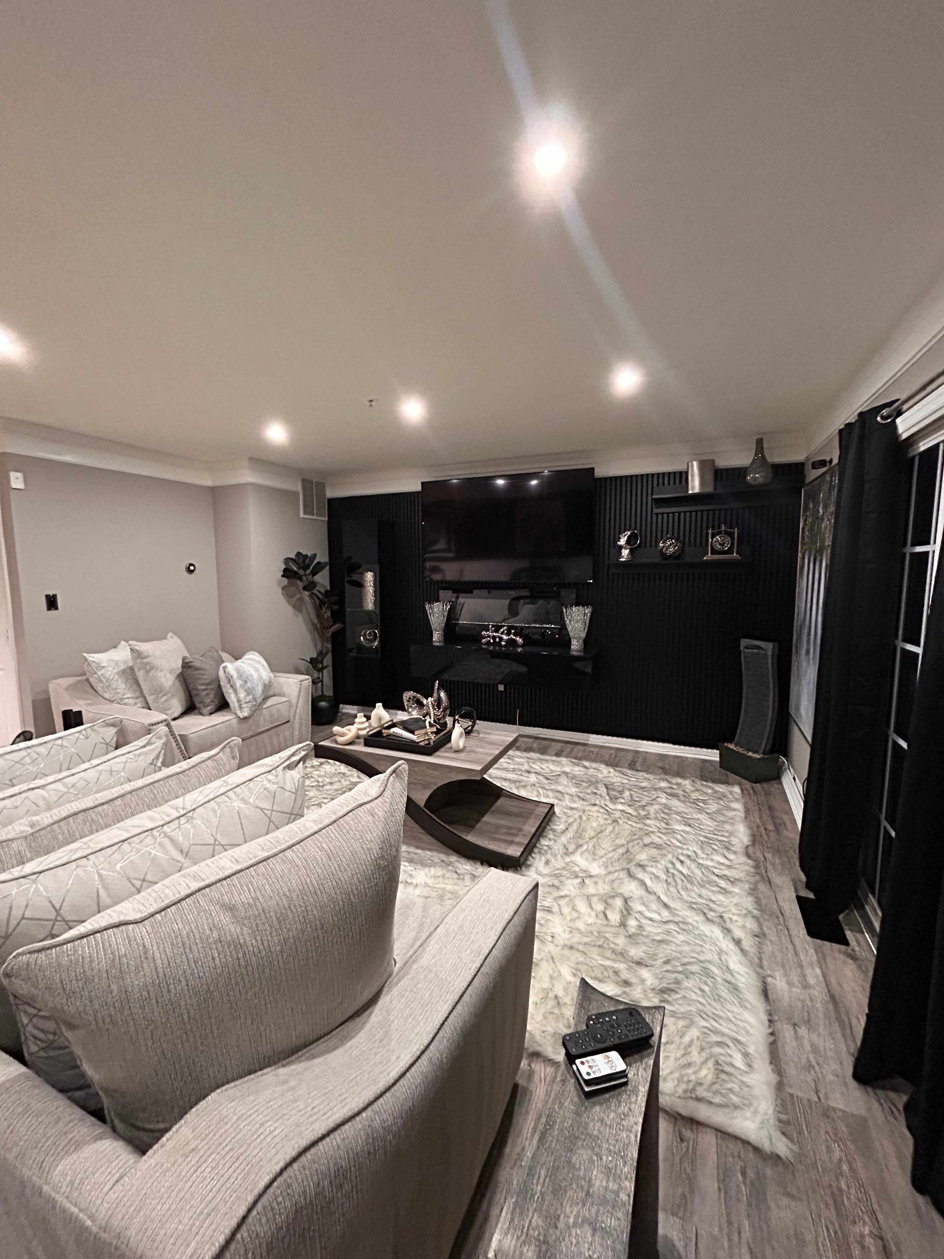 Contemporary living room featuring grey sofas, a shag rug, and a black slatted wall.